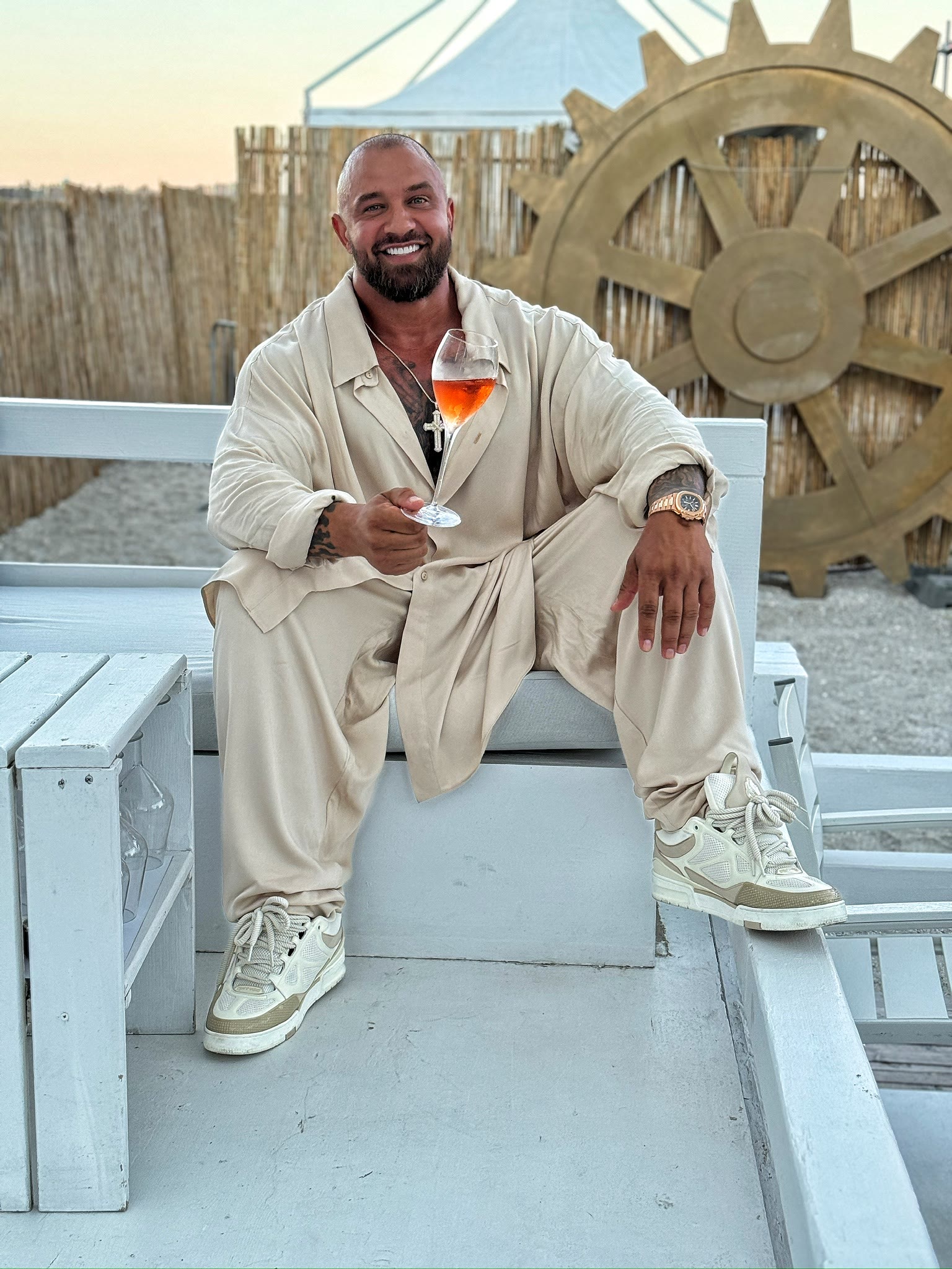 Alex Bodi seated with a drink in a light outfit